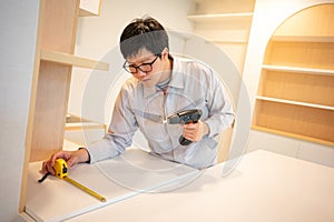 Asian male furniture assembler using tape measure