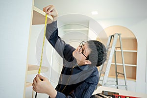 Asian male furniture assembler using tape measure