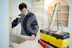 Asian male furniture assembler using tape measure