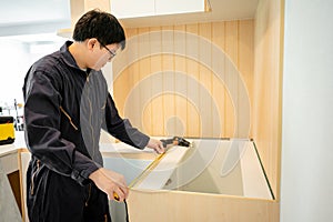 Asian male furniture assembler using tape measure