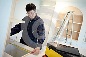 Asian male furniture assembler using tape measure