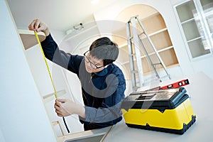 Asian male furniture assembler using tape measure