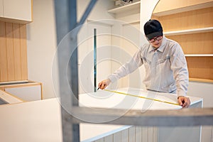 Asian male furniture assembler using tape measure