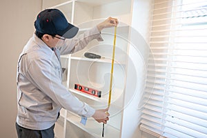 Asian male furniture assembler using tape measure on cabinet