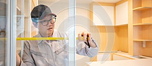 Asian male furniture assembler using tape measure on cabinet