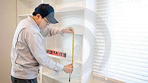 Asian male furniture assembler using tape measure on cabinet