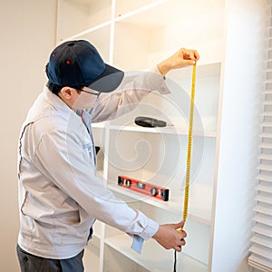 Asian male furniture assembler using tape measure on cabinet