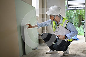 Asian male inspector wearing safety helmets and vest checking building structure with checklist in hand