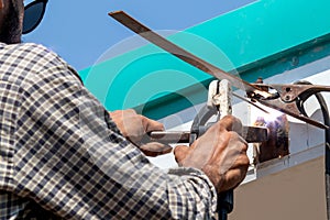 An Asian male laborer using a welding machine. To repair the roof of the house outdoors His hands held the welding machine with th