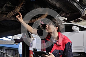 Asian male motor mechanic inspects undercarriage of EV car at service garage.