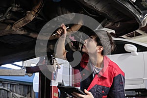 Asian male motor mechanic inspects undercarriage of EV car at service garage.