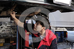 Asian male motor mechanic inspects undercarriage of EV car at service garage.