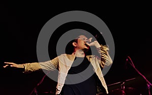 Asian male musical singer singing, celebrating, showing performance on stage in concert or event at night with spot light.