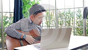 Asian male musician playing guitar in recording studio.