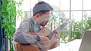 Asian male musician playing guitar in recording studio.