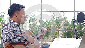 Asian male musician playing guitar in recording studio.