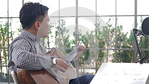 Asian male musician playing guitar in recording studio.