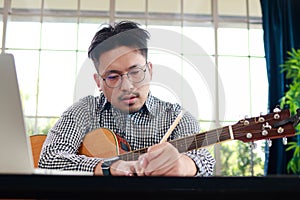 Asian male musician playing guitar in recording studio He is composing a song.
