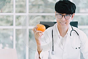 Asian male nutritionist holds an orange in his hand