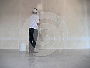 Asian male painter painting new white wall with roller brush, house interior renovation