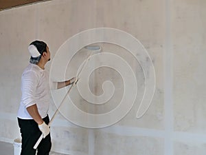 Asian male painter painting new white wall with roller brush, house interior renovation