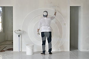 Asian male painter painting new white wall with roller brush, house interior renovation