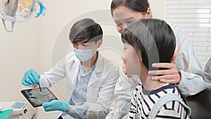 Asian male pediatric dentist explains teeth X-ray to a girl in a dental clinic.