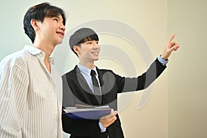 Asian male realtor wearing suit showing new house to smiling buyer. Real estate, loan and property investment concept