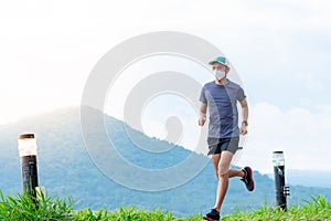 Asian male runners in blue shirts, sportswear, hats and masks are practicing running on a dirt road behind a mountain with a