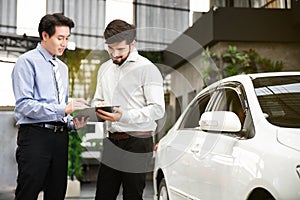 The Asian male salesperson talking and explaining about leasing and insurance to a smiling and happy Caucasian male client.