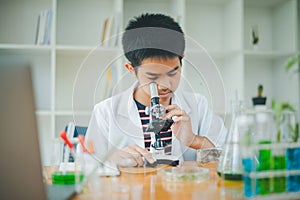 Asian male science students looking through a microscope and tests of plants in the classroom. Learning about scientific