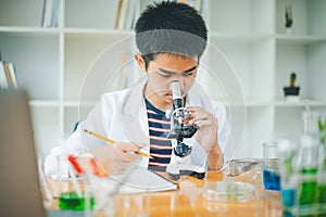 Asian male science students looking through a microscope and tests of plants in the classroom. Learning about scientific