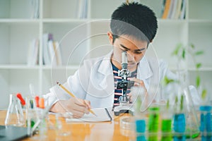 Asian male science students looking through a microscope and tests of plants in the classroom. Learning about scientific