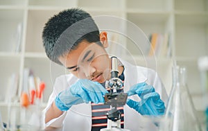 Asian male science students looking through a microscope and tests of plants in the classroom. Learning about scientific