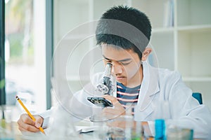 Asian male science students looking through a microscope and tests of plants in the classroom. Learning about scientific