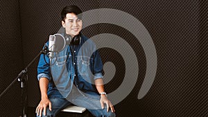 Asian male singer recording songs by using a studio microphone and pop shield on mic with passion in a music recording studio.