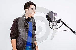 Asian male singer recording songs by using a studio microphone and pop shield on mic with passion in a music recording studio.