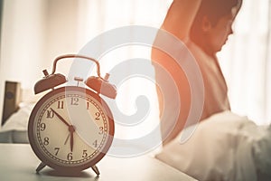 Asian male stretching out after woke up with alarm clock showing six o clock