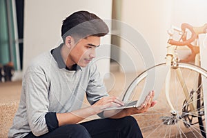 Asian male student sitting at the stairs and smiling as use laptop computer with his bike background at campus,Students and