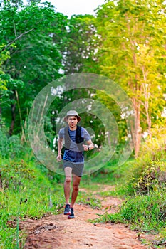 Asian male trail runner Wearing runners, sportswear, practicing running on a dirt path in a forest with trees behind