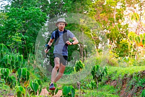 Asian male trail runner Wearing runners, sportswear, practicing running on a dirt path in a forest with trees behind