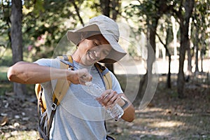 Asian male traveler carrying a large backpack drinks water from a bottle while resting during a hike.