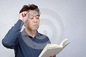 Asian male trying to read something in his book. poor sight, presbyopia, myopia