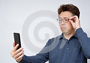 Asian male trying to read something on his mobile phone. poor sight, presbyopia, myopia