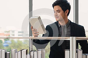 Asian male university students standing at bookshelf seaching and reading book in library