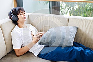 Asian Male using smartphone while listening to music at home. Time to relax and leisure activities