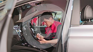 Asian male worker checking a maintenance list with tablet in a car interior.