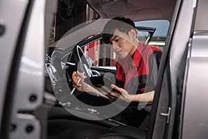 Asian male worker checking a maintenance list with tablet in a car interior.