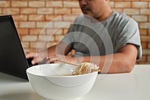 Asian male worker hastily eats instant noodles at busy overtime work