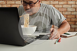 Asian male worker hastily eats instant noodles at busy overtime work